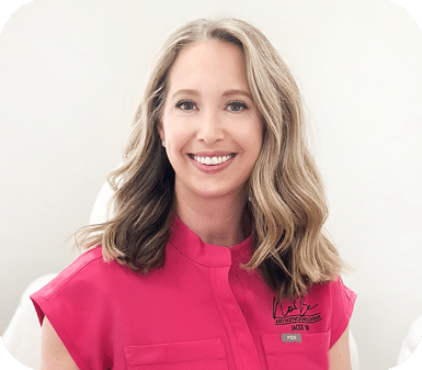 Portrait of a smiling woman with shoulder‑length blonde hair wearing a pink uniform shirt with a logo on the chest.